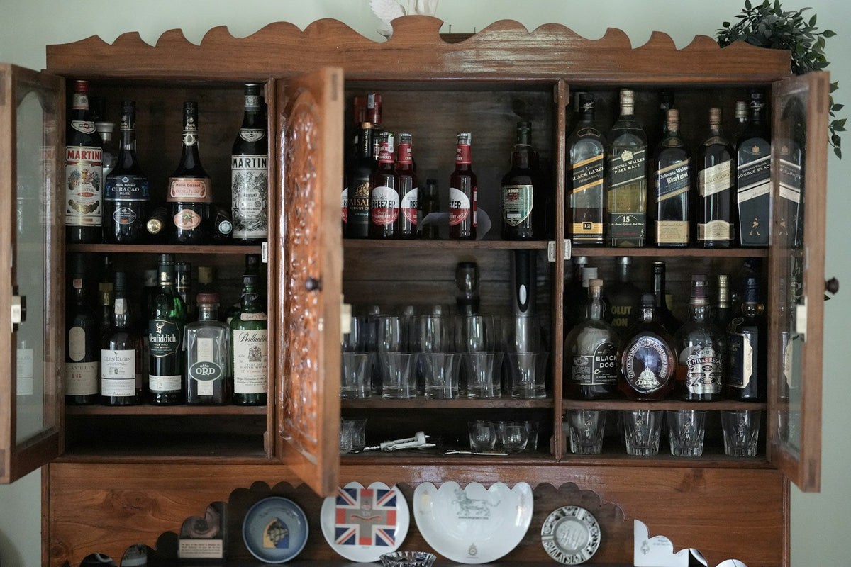 Wooden home bar cabinet filled with wine bottles and glasses