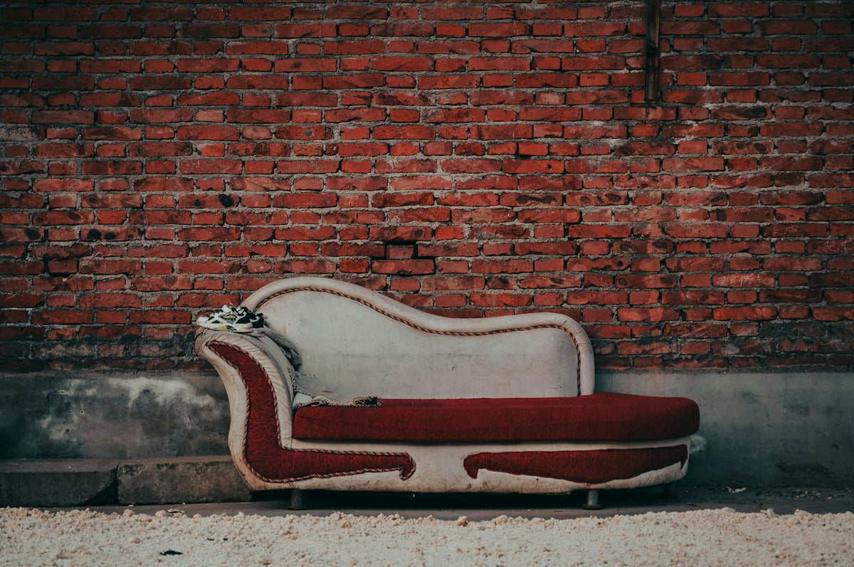 Antique upholstered chaise lounge against a warm brick wall